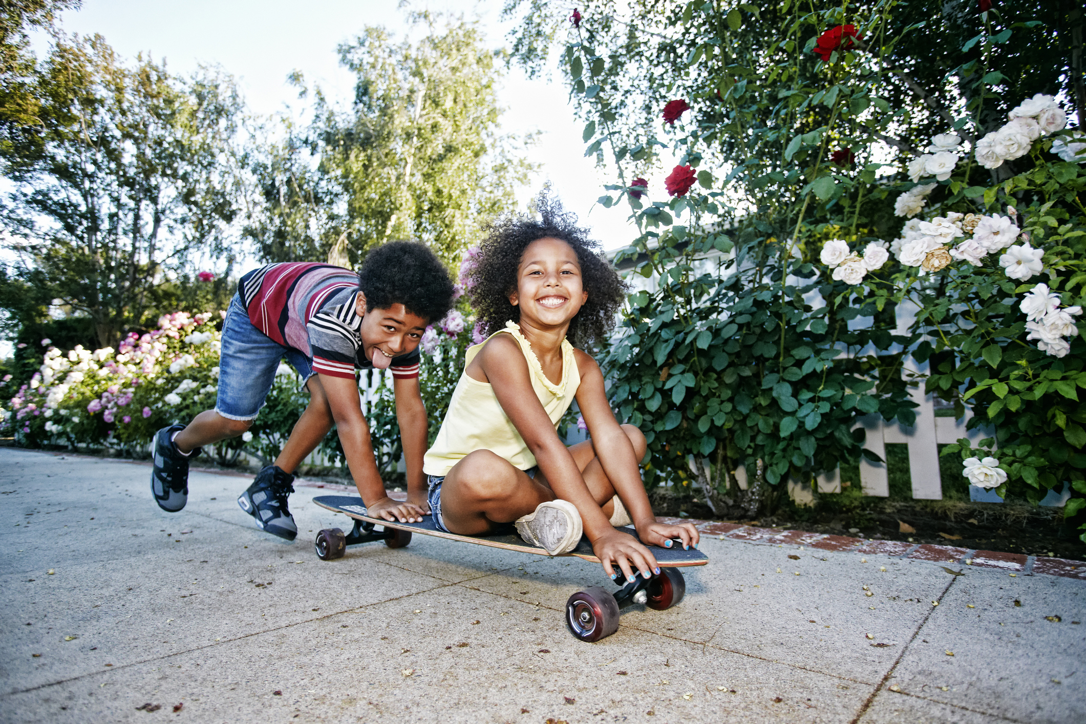 mixed-race-boy-pushing-sister-on-skateboard-on-sidewalk